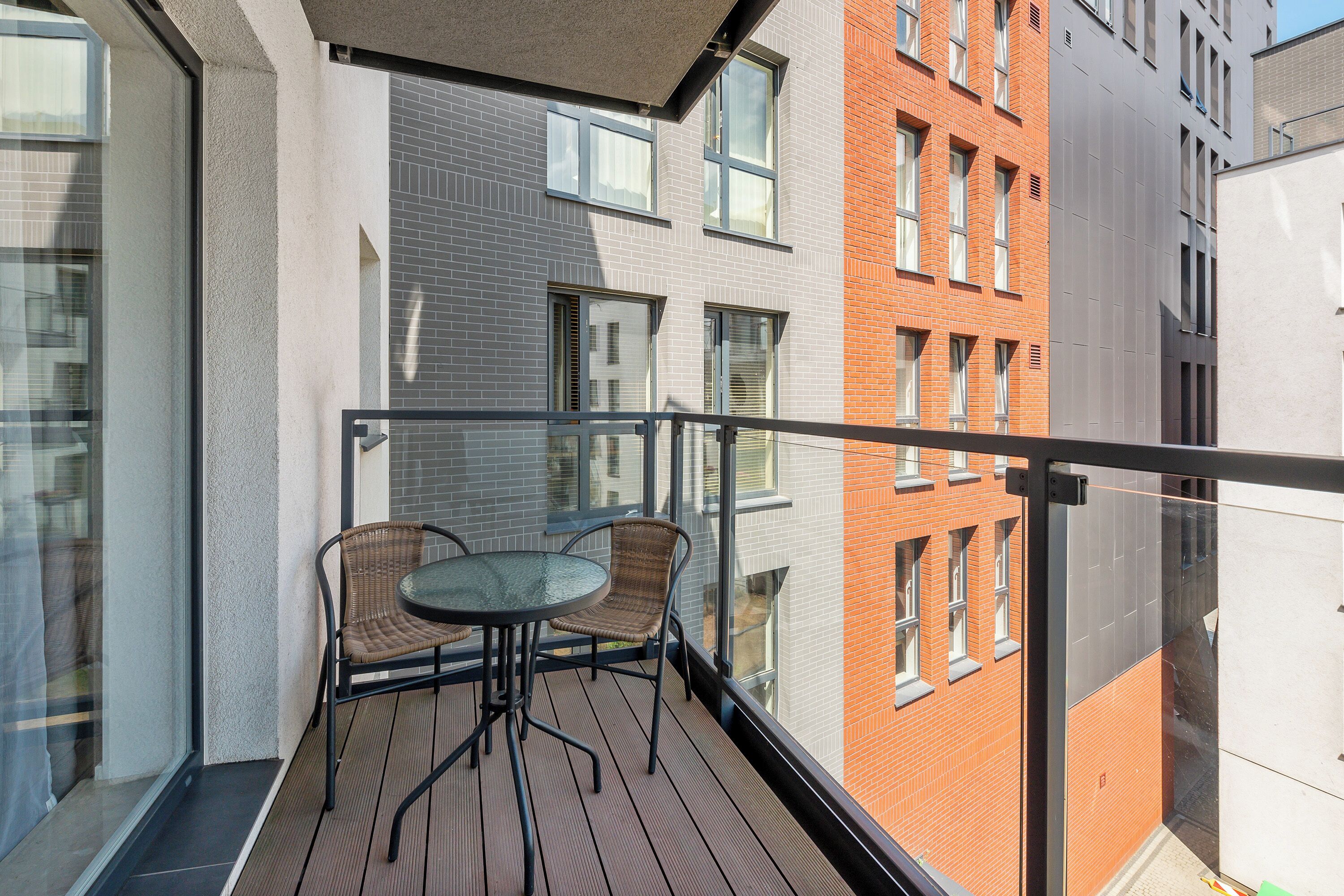 En balkon med et bord og stole, med udsigt over en bygning i en blanding af mursten og moderne stil.