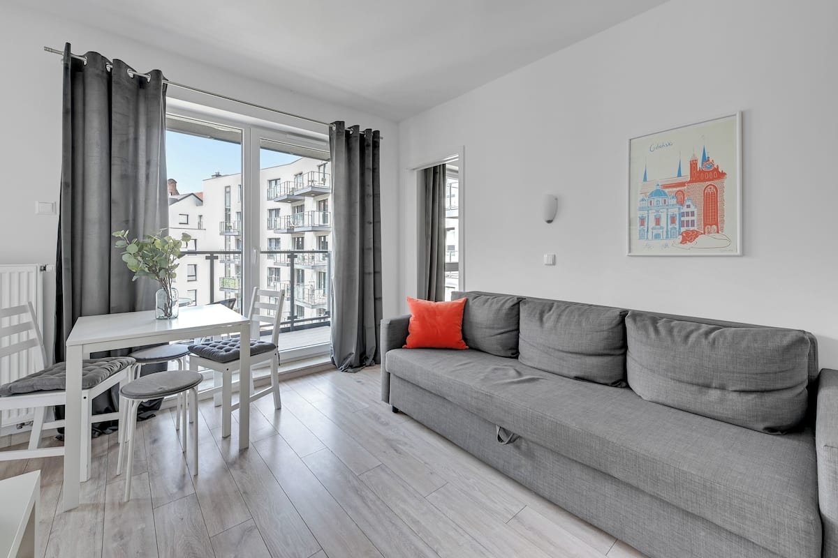 A modern living room with a grey sofa, white dining table, and grey curtains.