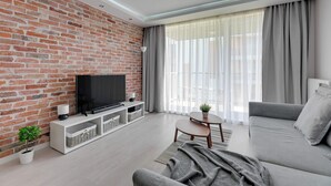 Un salón moderno con pared de ladrillo, un televisor de pantalla plana, un sofá gris y una mesita con una planta.