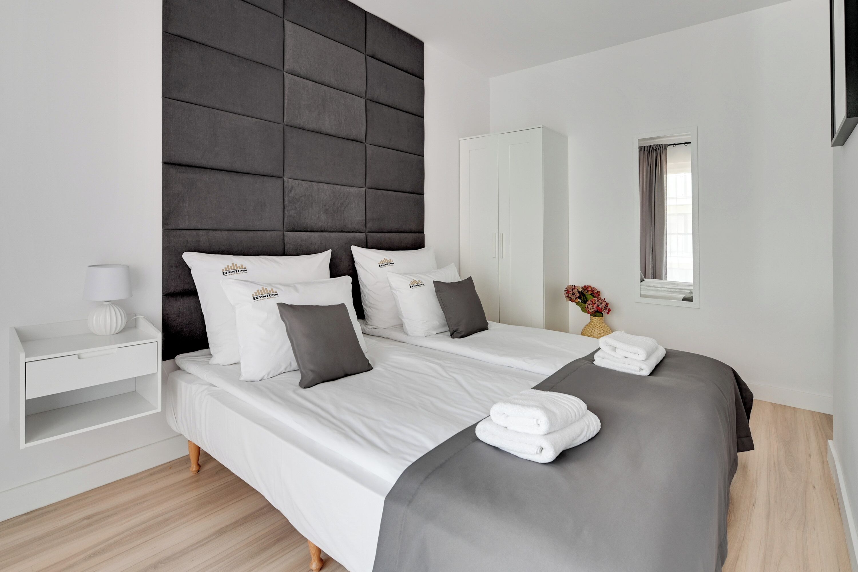 Una habitación de hotel moderna con una cama grande, un armario, una mesita de noche y una ventana con cortinas.