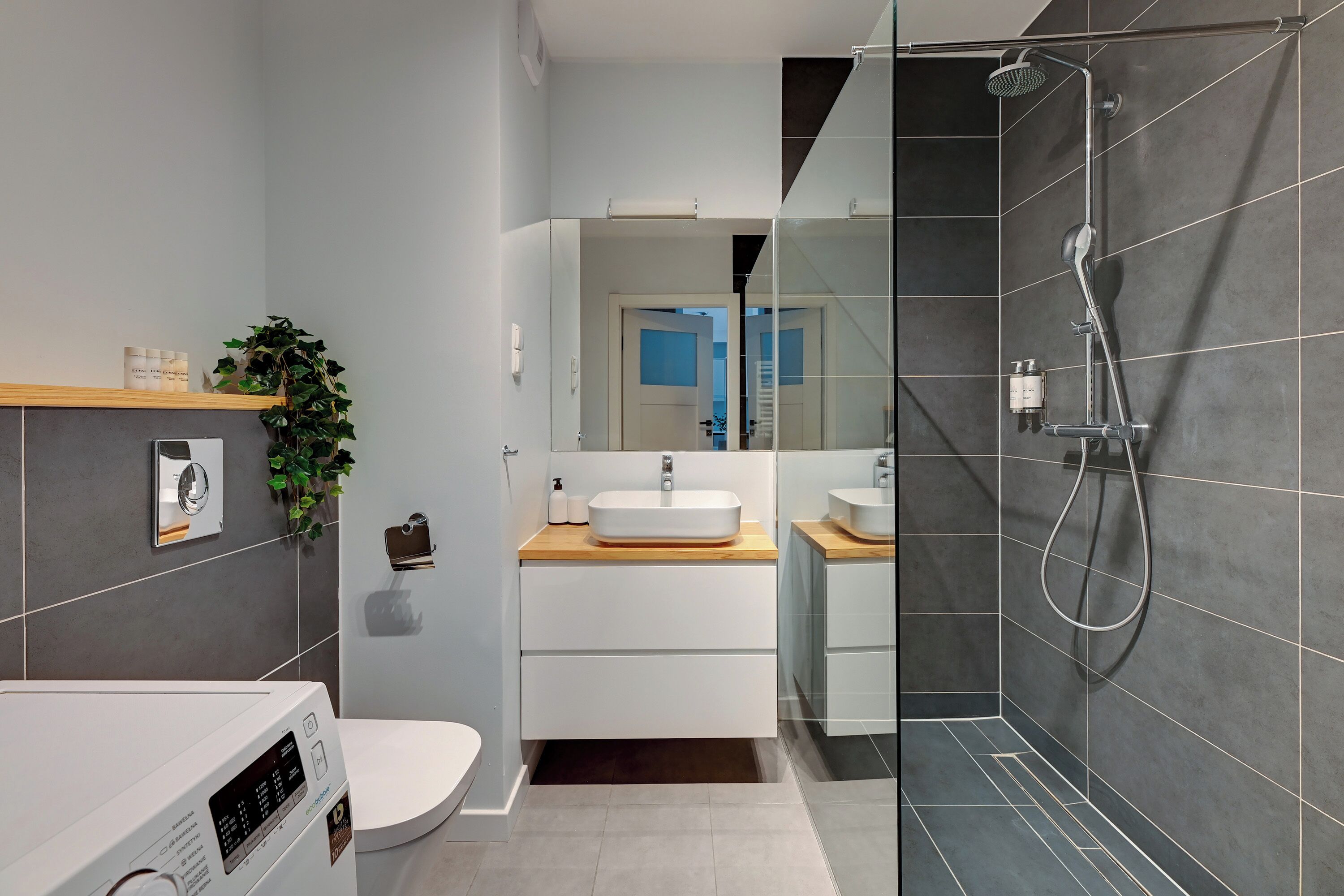 A modern bathroom with a white toilet, a sink with a wooden countertop, a mirror, and a glass-enclosed shower area.