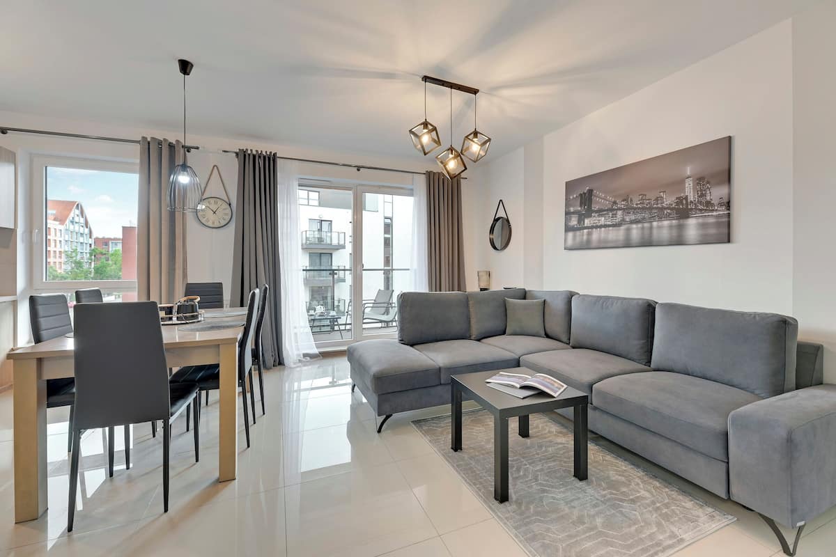 A modern living room with a grey sofa, a dining table with chairs, a coffee table, and a cityscape painting on the wall.