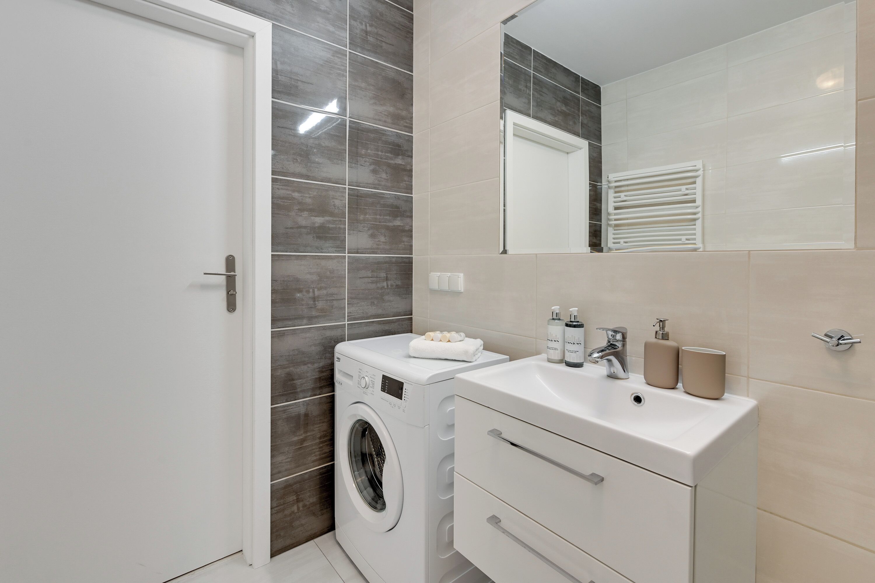 Une salle de bain moderne équipée d’un lave-linge, d’un évier et d’un miroir.