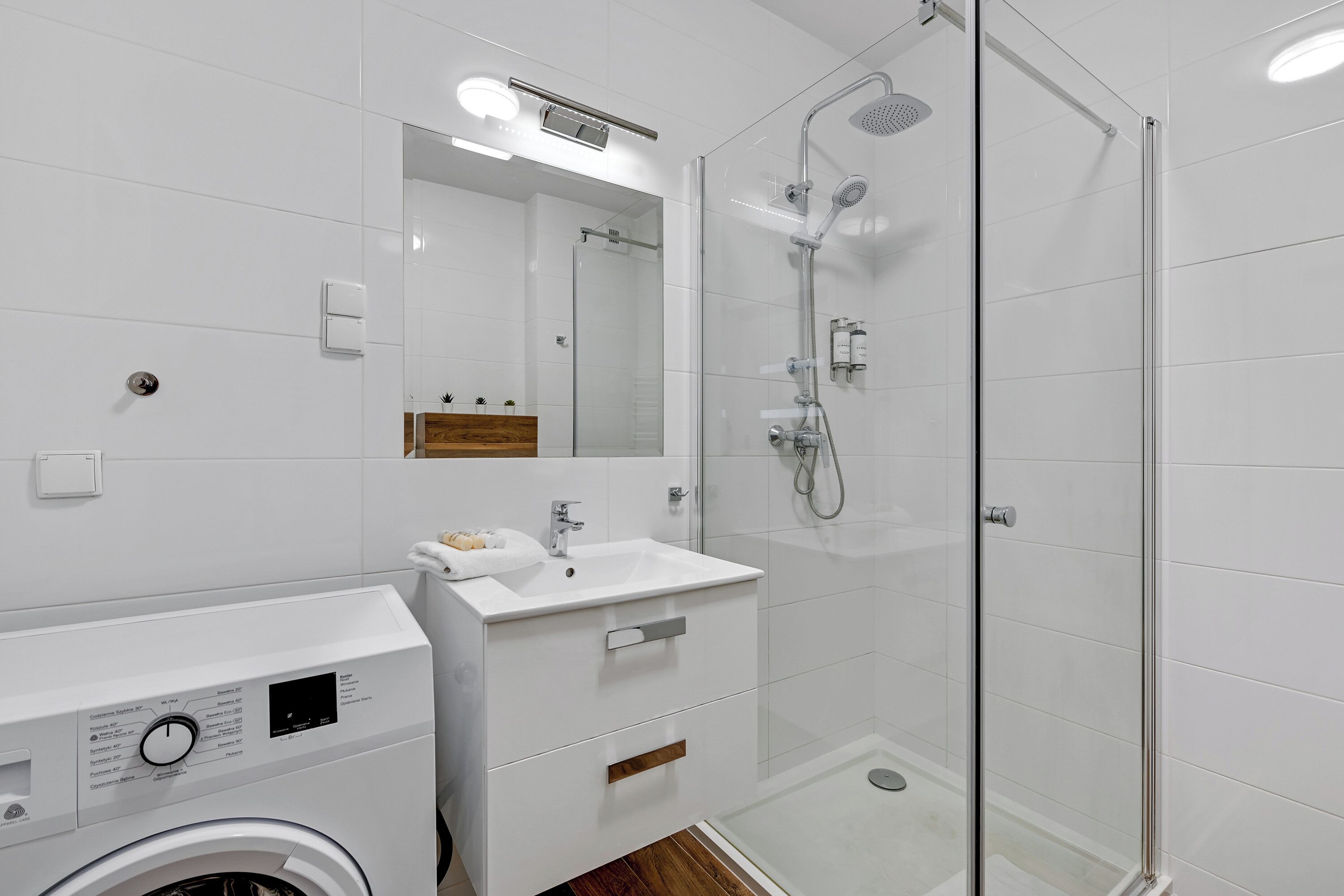 A modern bathroom with a washing machine, a sink, and a glass-enclosed shower area.