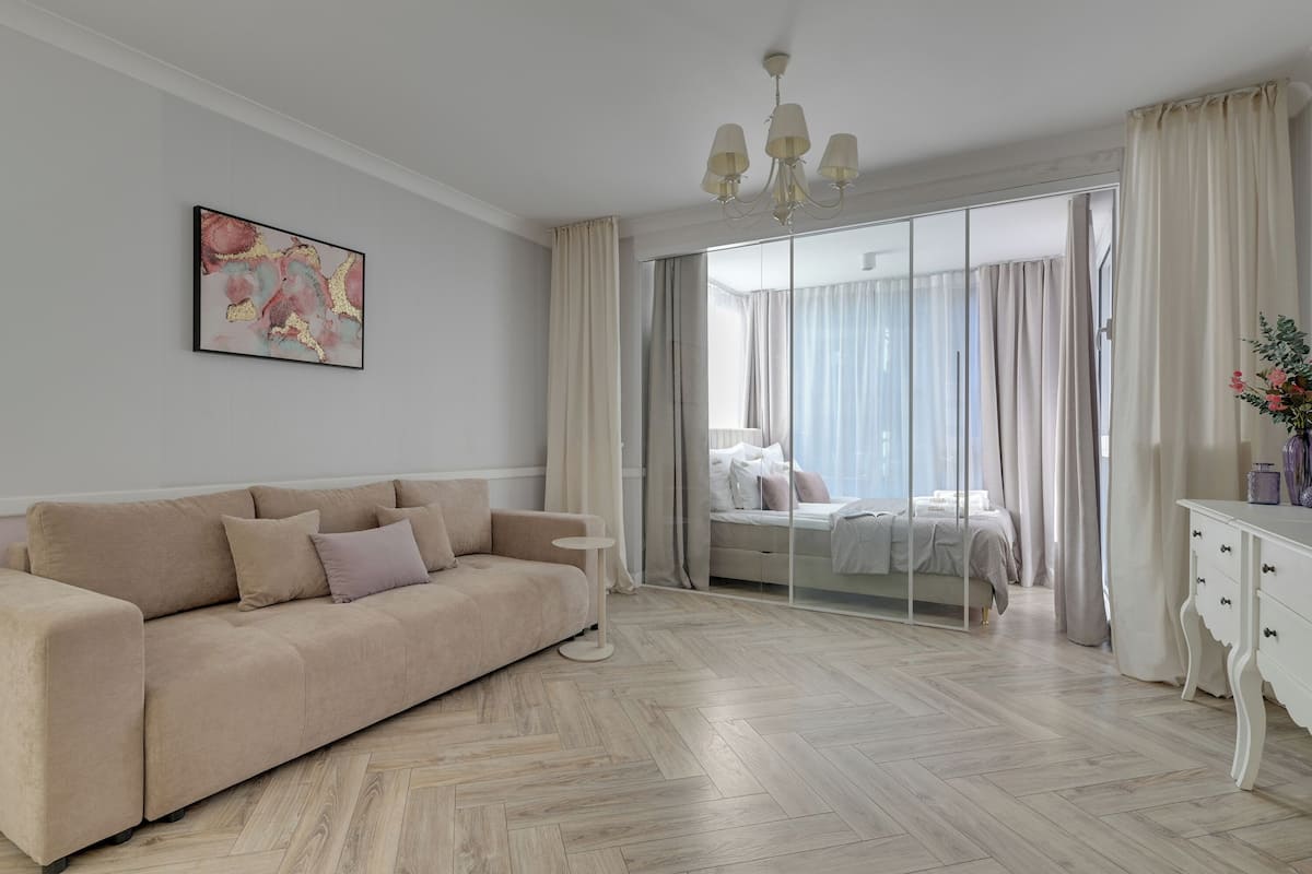 A modern bedroom with a sofa, a bedside table, a dresser, and a large window with curtains.