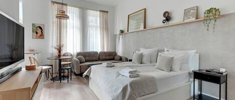 Un dormitorio moderno con cama, mesita de noche, televisor y una zona de estar con mesa y sillas.