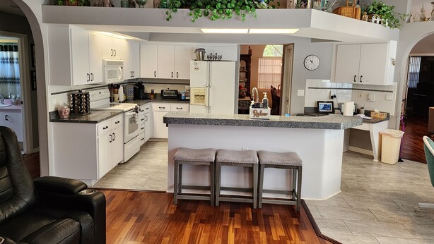 A modern kitchen with white cabinets, a central island, and a dining area visible through an open door. - Special summer discounts available NOW! Family-Friendly Heated Pool Escape (Land O' Lakes)