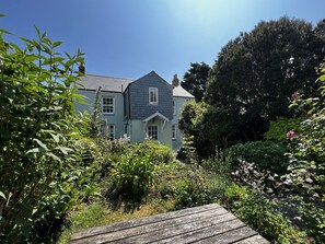 A house with a grey roof and a green facade, surrounded by lush greenery and a wooden deck. - Sparrows Nest - Three Bedroom Cottage, Sleeps 6 (Paul)