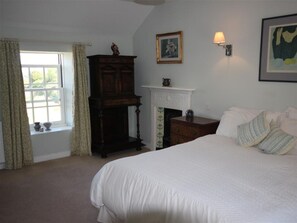 A bedroom with a large bed, a dresser, a fireplace, and a window with curtains. - Sparrows Nest - Three Bedroom Cottage, Sleeps 6 (Paul)