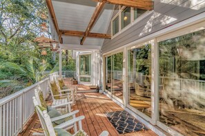 Una terraza cubierta con sillas blancas, una mesa de madera y grandes puertas de cristal que dan a un jardín.