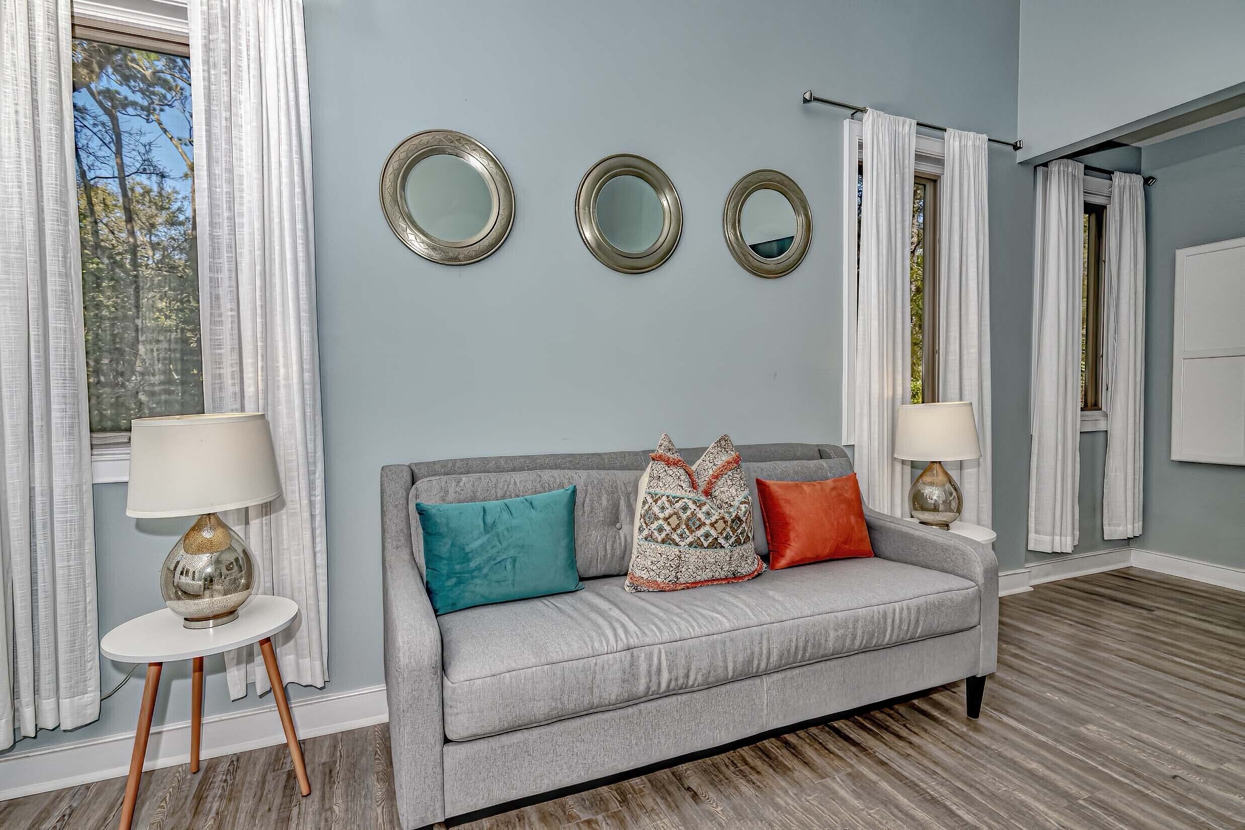 A living room with a grey sofa, three wall mirrors, and two lamps on side tables.