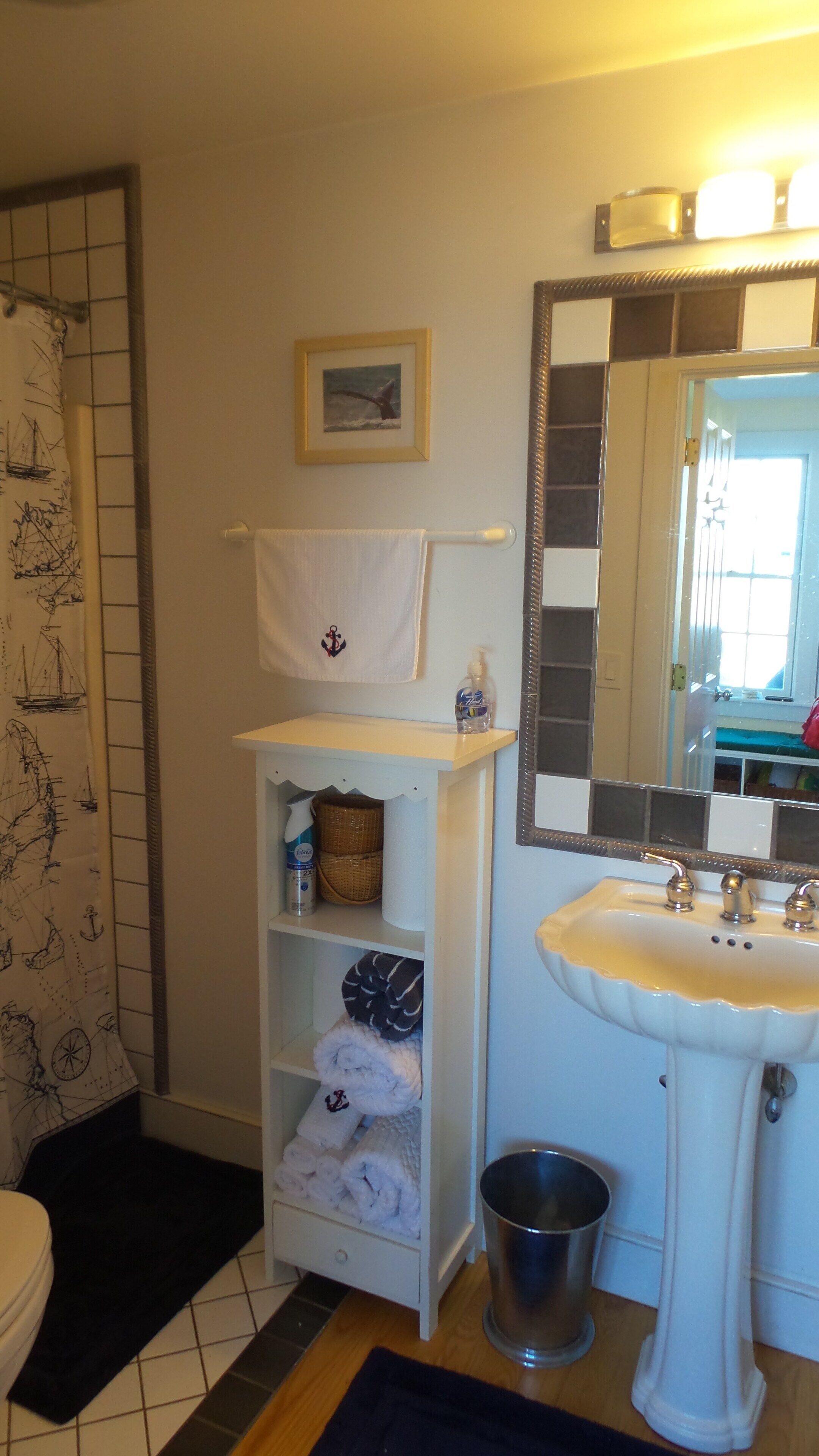 A bathroom with a white sink, a mirror, a towel rack, a shelf with towels and toiletries, and a shower curtain with nautical designs.