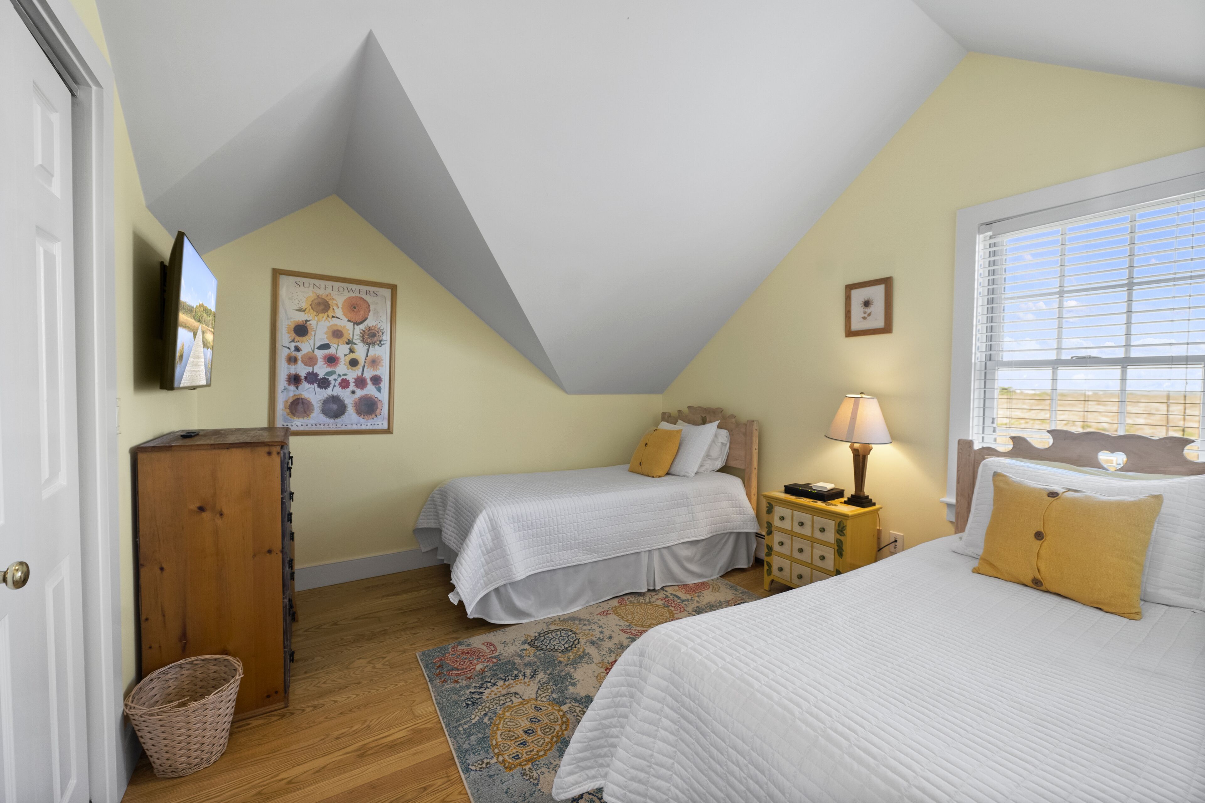 A bedroom with two single beds, a wooden cabinet, a television, and a window with blinds.