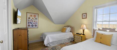 A bedroom with two single beds, a wooden cabinet, a television, and a window with blinds.