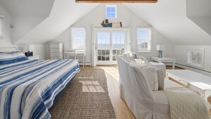 A bedroom with a sloped ceiling, a bed with a striped bedspread, a bedside table, a chair, and a window with a view.