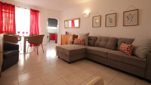 Ein Wohnzimmer mit einer Couch, einem Esstisch mit Stühlen und einer Küche im Hintergrund.