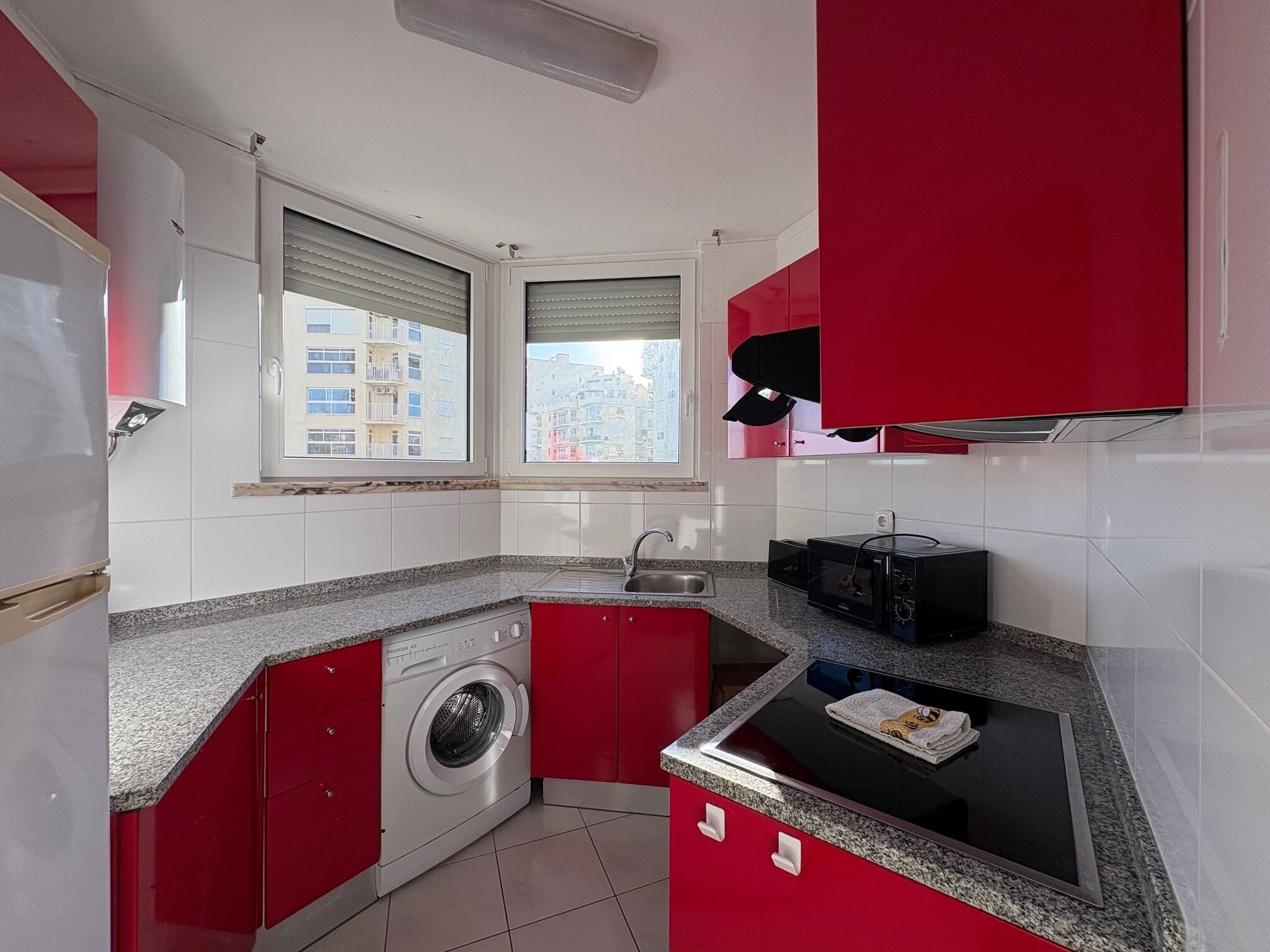 A compact kitchen with red cabinets, a washing machine, a microwave, and a sink.