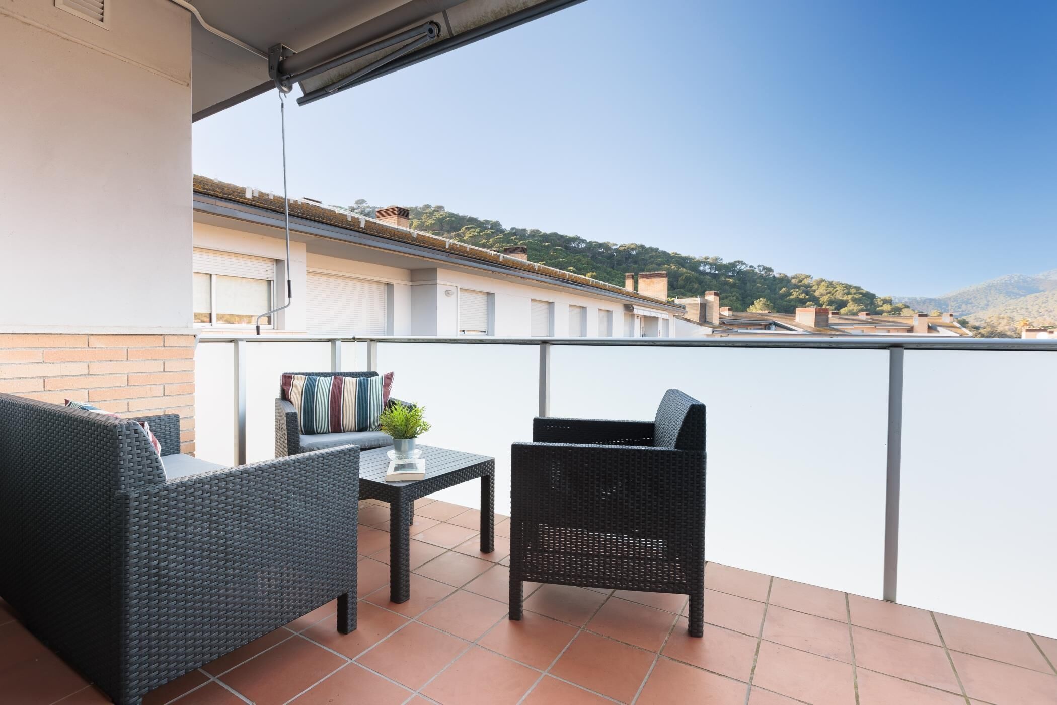 A balcony with a wicker sofa, a small table, and a chair.