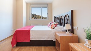 Een slaapkamer met een bed, nachtkastje, lamp en uitzicht op het buiten.