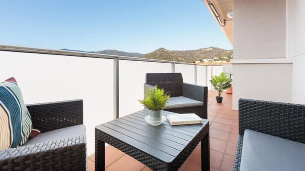 Een balkon met rieten meubels, een tafeltje met een plant en een boek.