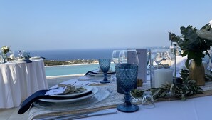 Taula preparada per a dinar amb vista al mar, amb vetreria blava i estovalls blancs.
