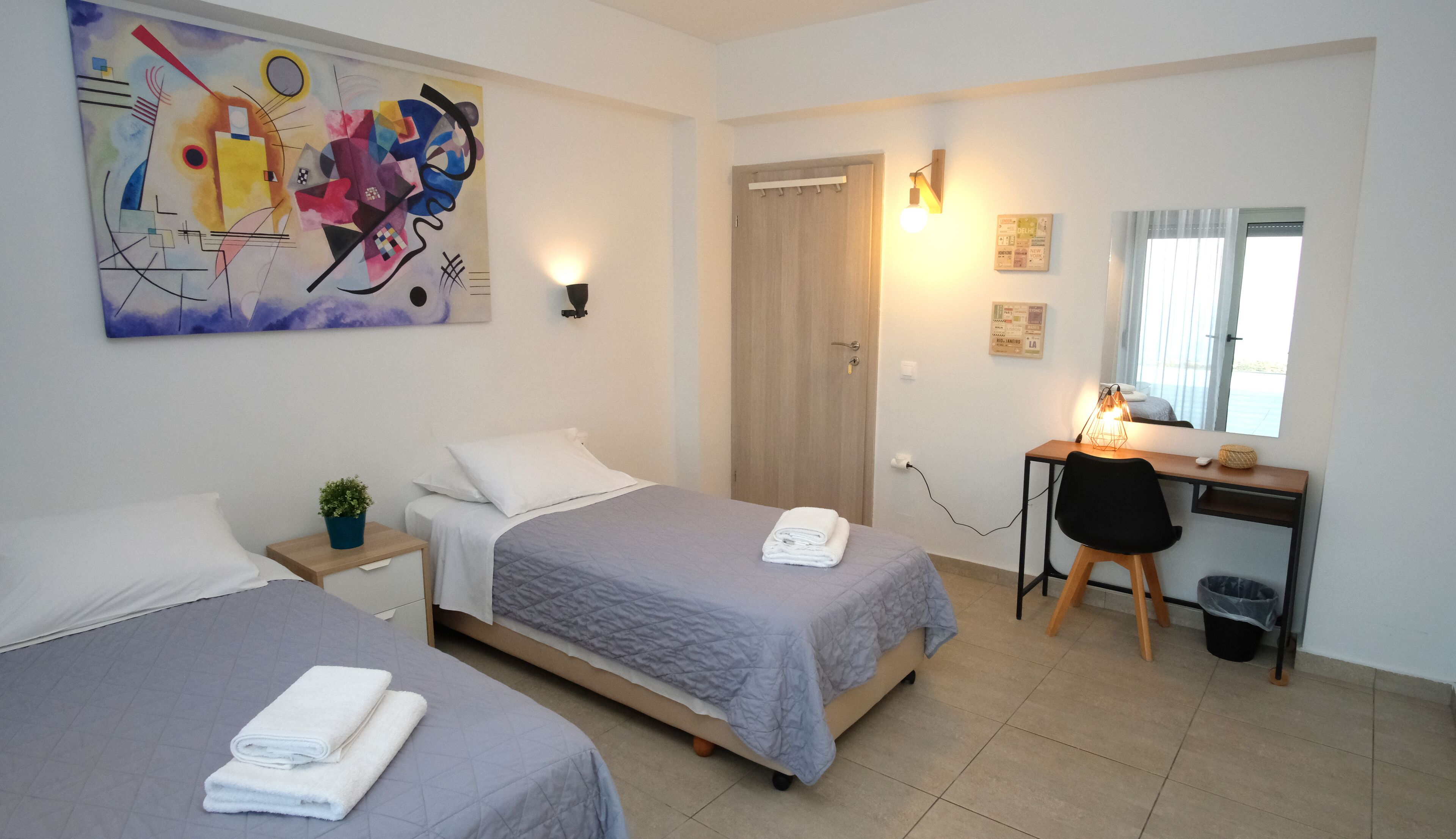 Ein Hotelzimmer mit zwei Betten, einem Schreibtisch, einem Stuhl, einer Lampe und einem Bild an der Wand.
