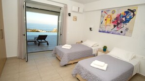 Habitació d'hotel amb dos llits, un balcó amb vista al mar, un quadre a la paret i un aparell d'aire condicionat.