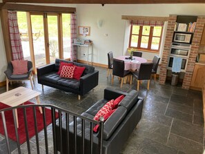 A spacious living area with a black leather sofa, a dining table with chairs, and a kitchen area with a microwave and oven.