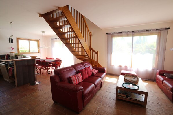 A spacious living area with a red leather sofa, a wooden staircase, and a dining area with a table and chairs. - House / Villa - Baden (Baden)