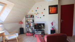 A cozy room with a sloped ceiling, a bookshelf, a television, a red door, and a window.