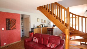 A living room with a red leather sofa, wooden staircase, and a kitchen area in the background.
