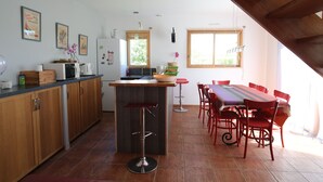 A modern kitchen with wooden cabinets, a central island, and a dining area with red chairs.
