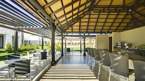 Un espace extérieur aménagé avec des sièges, un toit de chaume, des chaises modernes et une vue sur un bâtiment en arrière-plan.