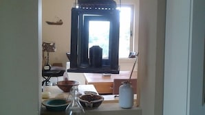 Un pasillo estrecho con una lámpara colgante, una ventana con persianas y una mesa con varios objetos, incluyendo una botella de vidrio y recipientes.