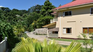A two-story building with a red roof, a stone wall, and a balcony. - Zeph Selfcatering (Mahé Island)
