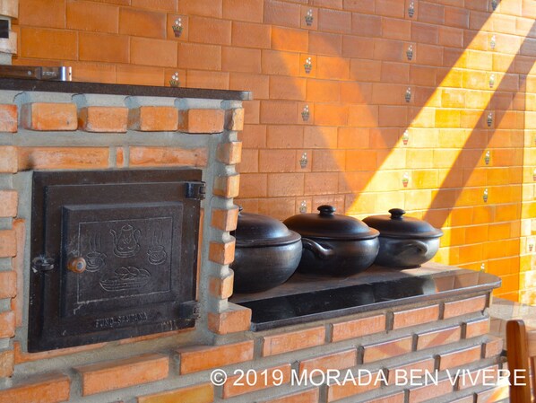 Un four en briques avec des casseroles sur une étagère, une porte en métal avec une poignée et un mur carrelé orné de plantes en pot.