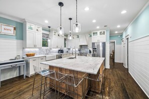 A modern kitchen with a marble island, wooden bar stools, and pendant lighting.
