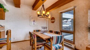 Comedor con mesa de madera y sillas tapizadas a rayas, una araña y vistas al exterior a través de un ventanal grande.