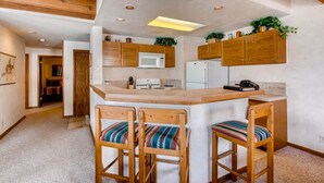 Cocina compacta con armarios de madera, una isla central y taburetes de bar.