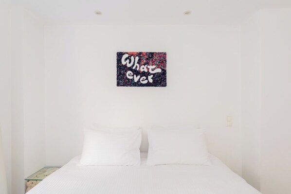A bedroom with a bed, two pillows, a small bedside table, and a wall-mounted artwork with the text 'What ever'. - Central Comfy Apt with Private Balcony & Rooftop Access. CT3 (Athens)