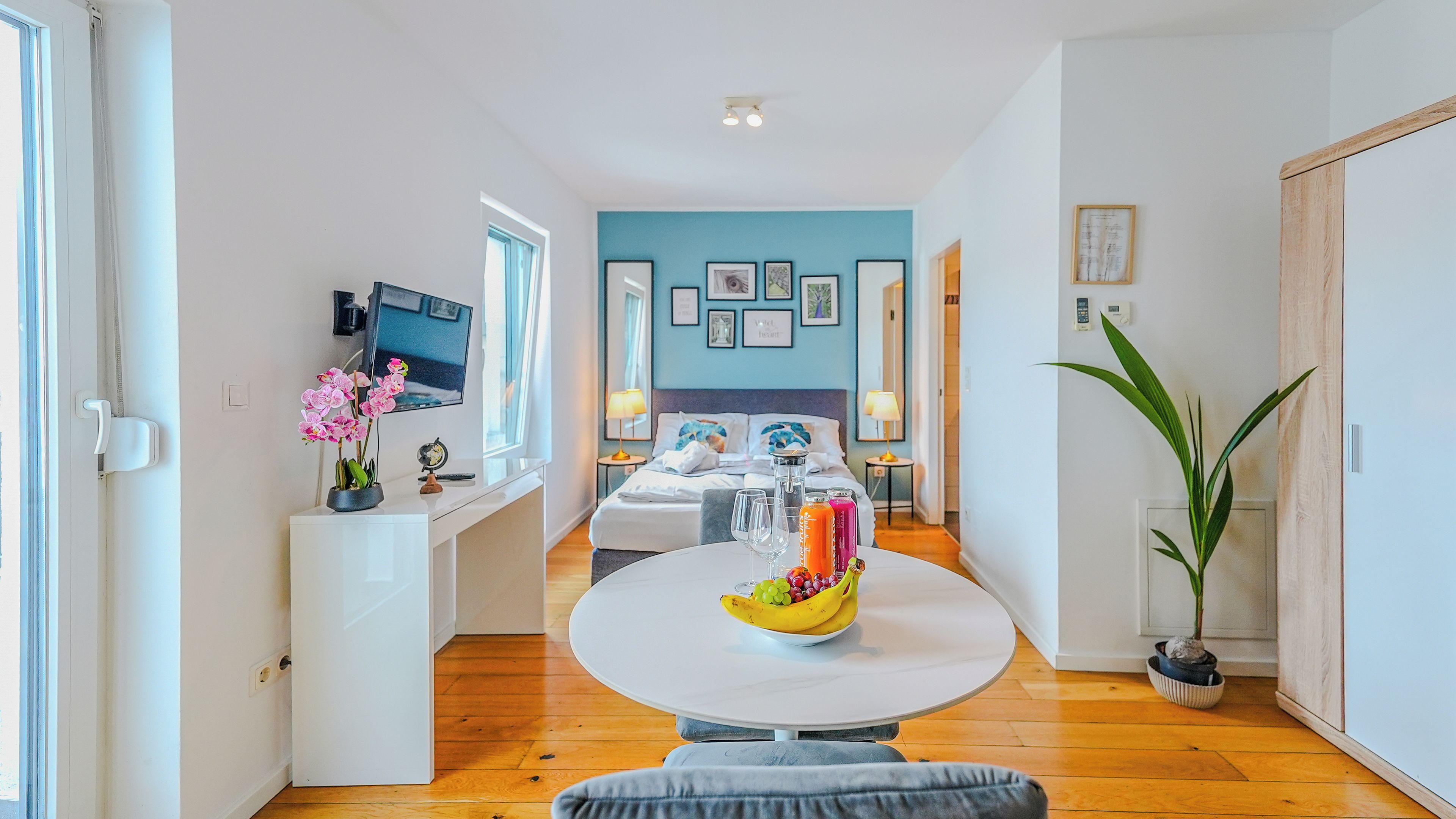 A modern hotel room with a bed, bedside table, and a dining area with a table set for two.