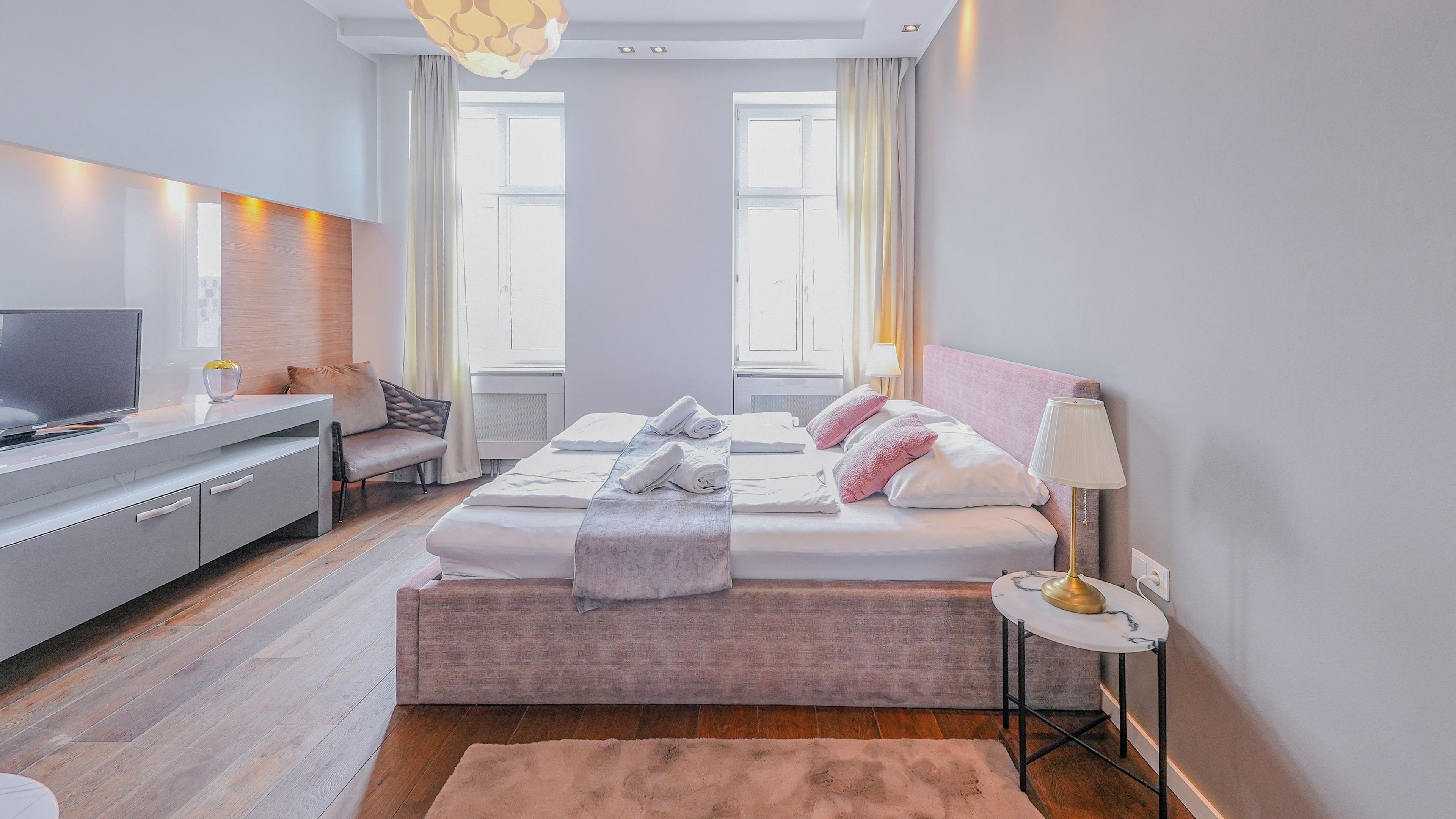 Ein modernes Hotelzimmer mit Bett, Nachttisch, Lampe und Schreibtisch mit Fernseher.