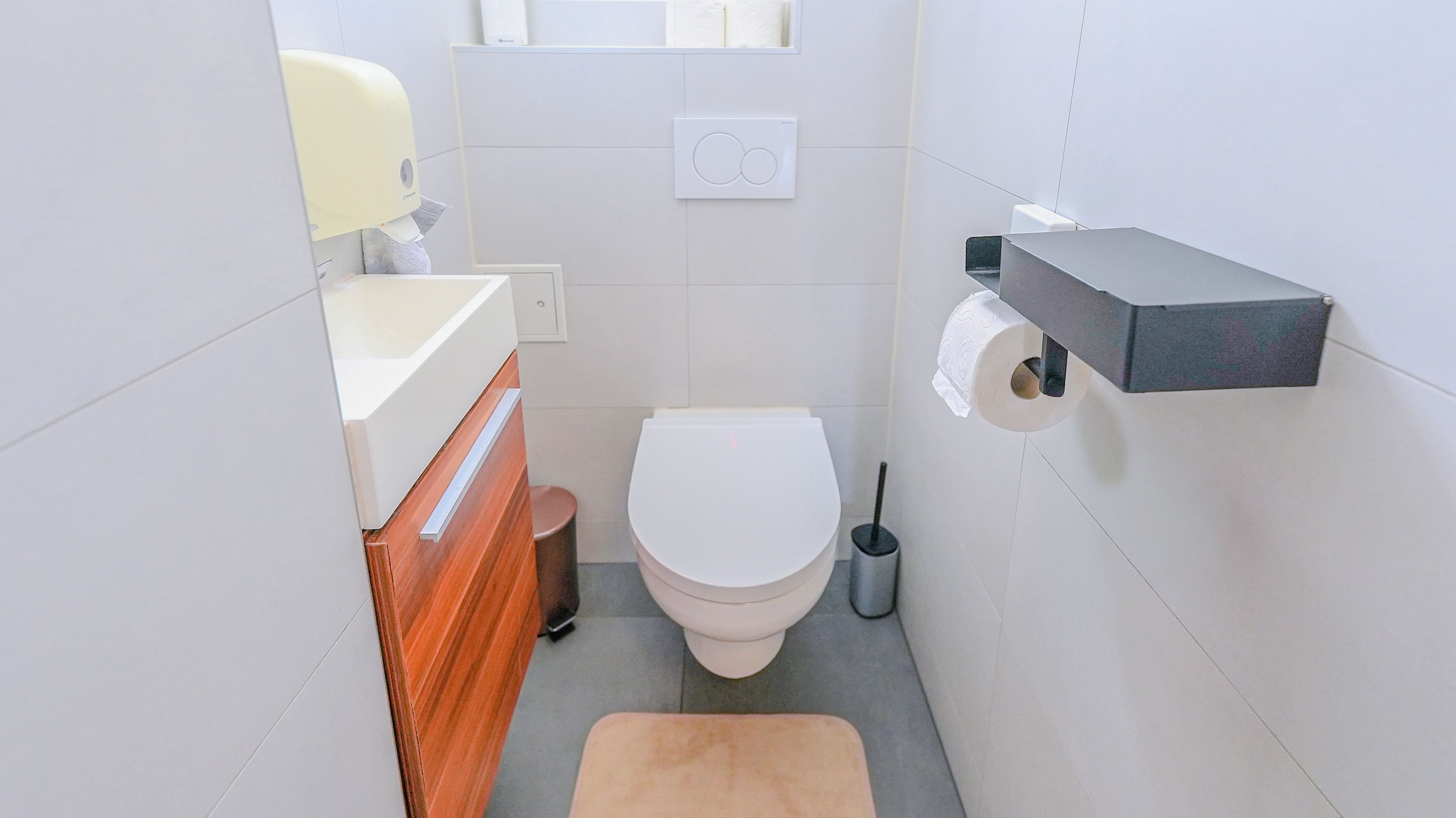 A compact bathroom with a toilet, a sink, a towel dispenser, and a toilet paper holder.