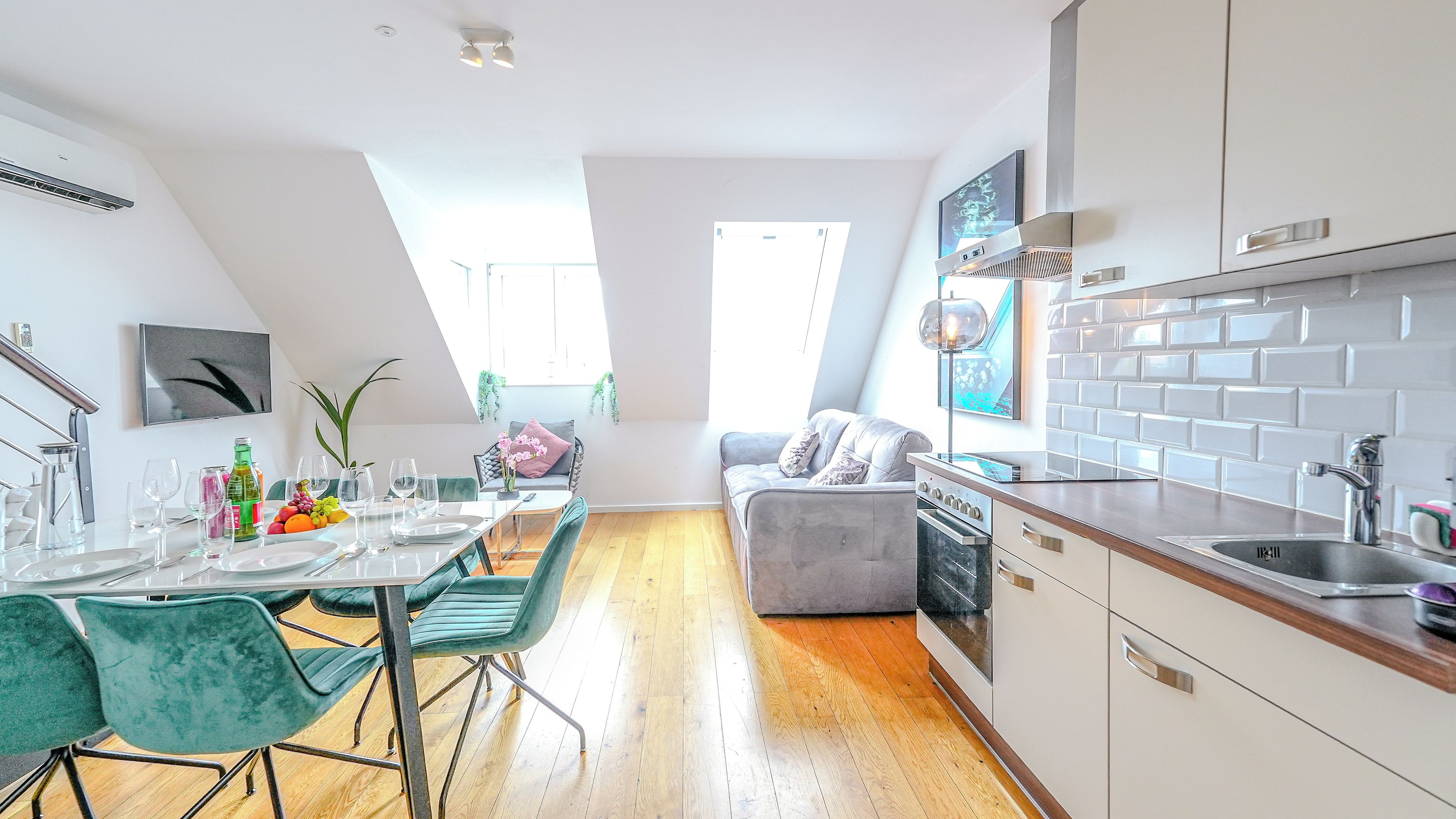 Een moderne keuken met een inbouwoven, een eethoek met een tafel voor vier personen, en een grijze bank op de achtergrond.
