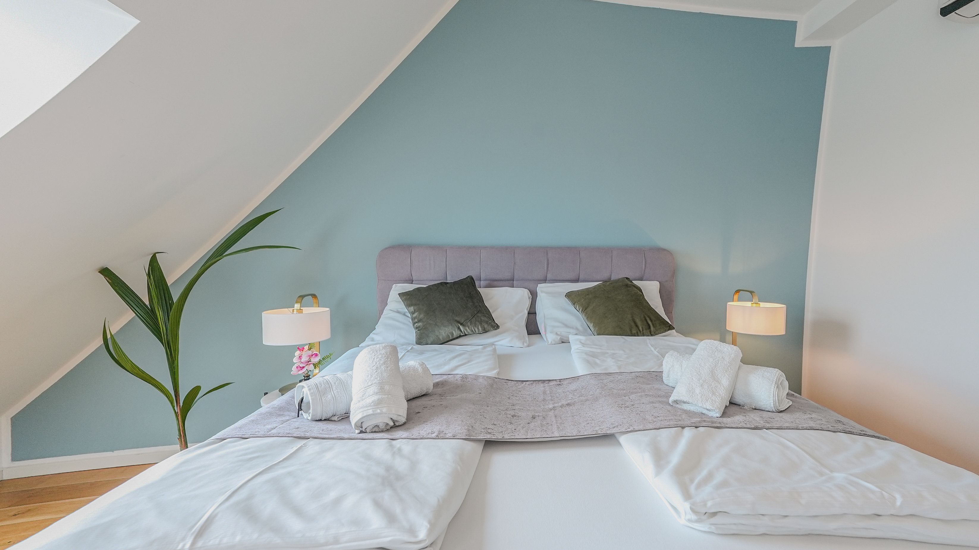 A neatly made bed with pillows, a bedside lamp, and a plant in a room with a sloped ceiling.
