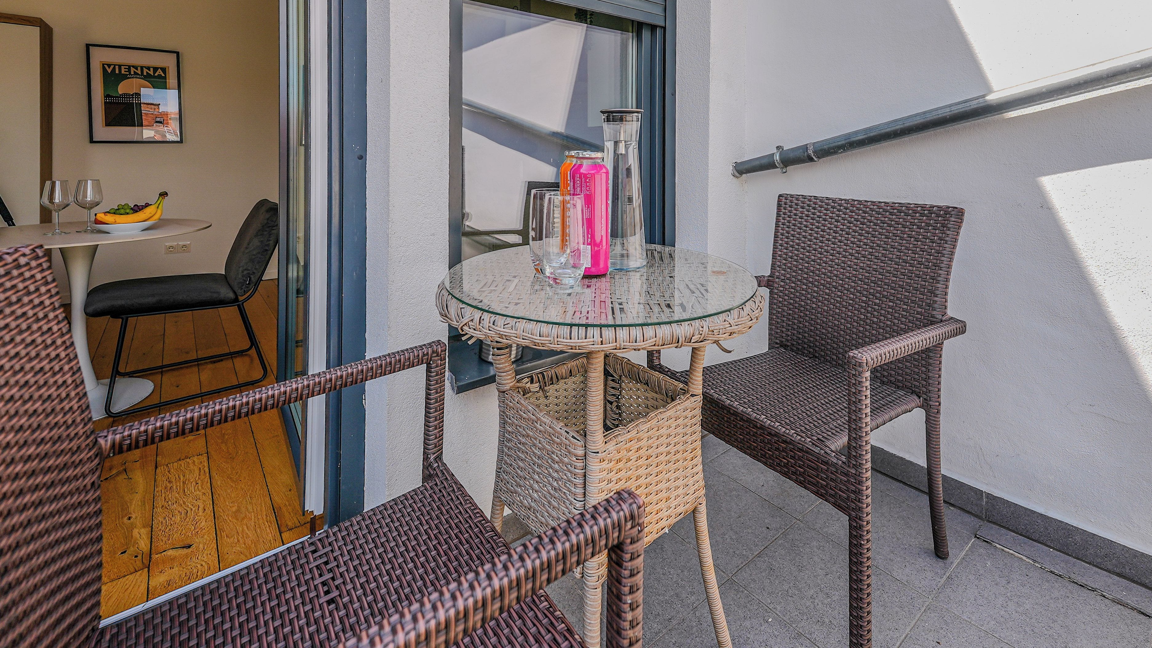A wicker chair and table set on a balcony with a glass top, a bottle, and a glass on the table.