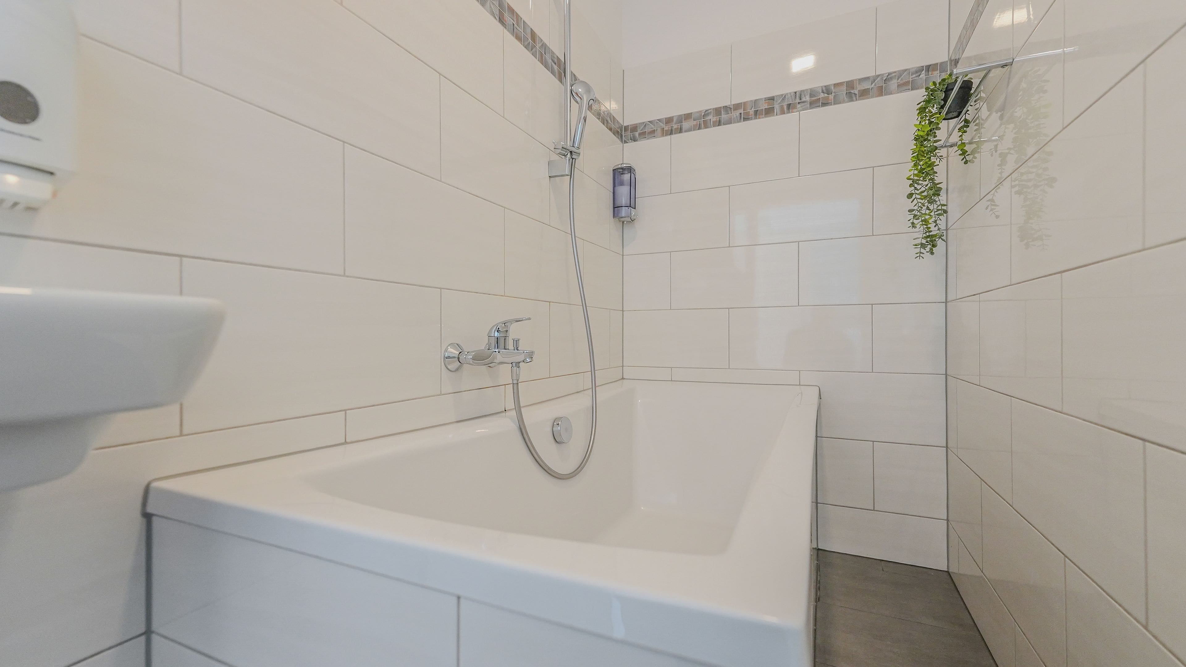 Ein modernes Badezimmer mit einer weißen Badewanne, einer Handbrause und einem am Wand montierten Wasserhahn.