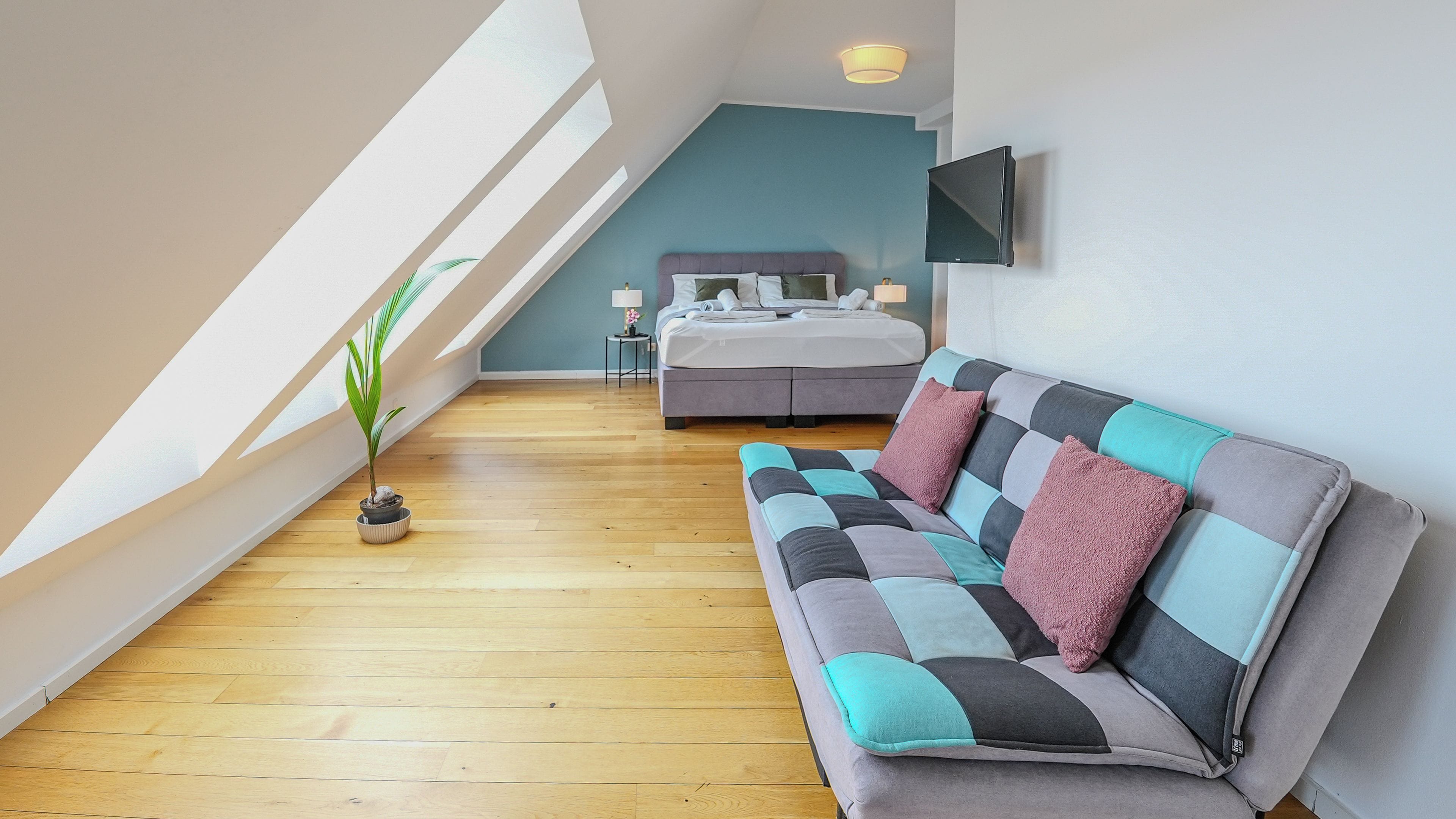 Een moderne slaapkamer met een schuine kap, een bed, een bank en een televisie.