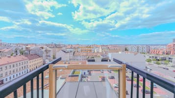 Une vue panoramique sur une ville, prise depuis un point d’observation élevé, avec différents types de bâtiments, un ciel dégagé et un parking situé en contrebas.