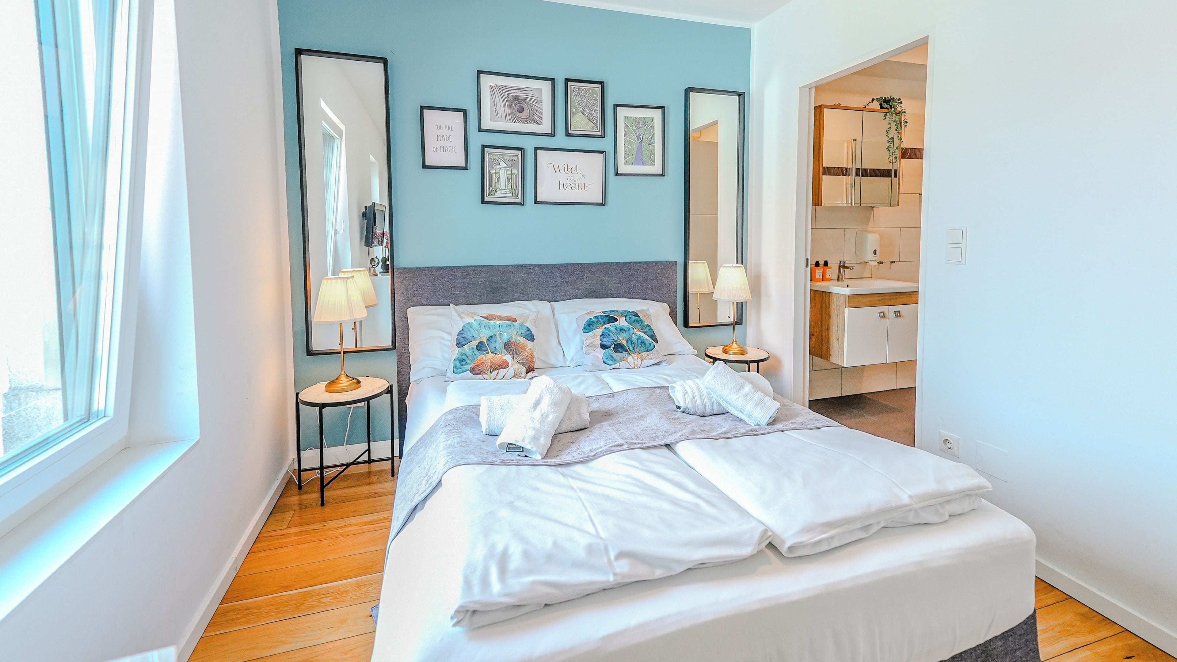 A modern bedroom with a bed, bedside tables, a mirror, and artwork on the wall.